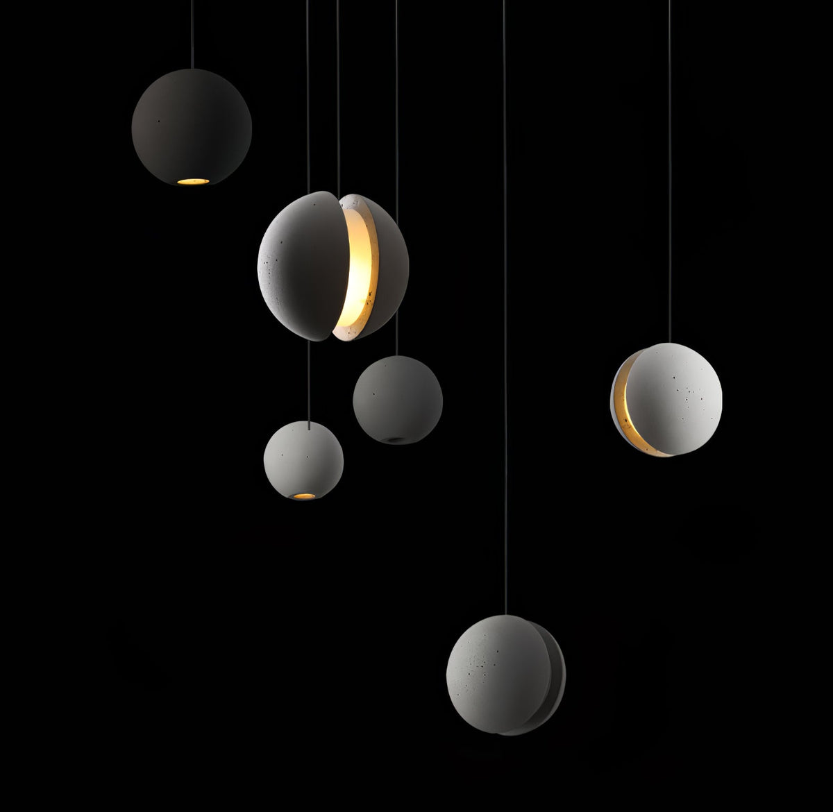 Six Clérachic concrete spheres float at different heights on a black backdrop, some glowing warmly through a slot or from the base.
