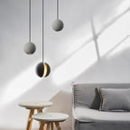 Close to the camera, a Clérachic concrete pendant glows through its slot, with two plain spheres behind and a grey sofa below.