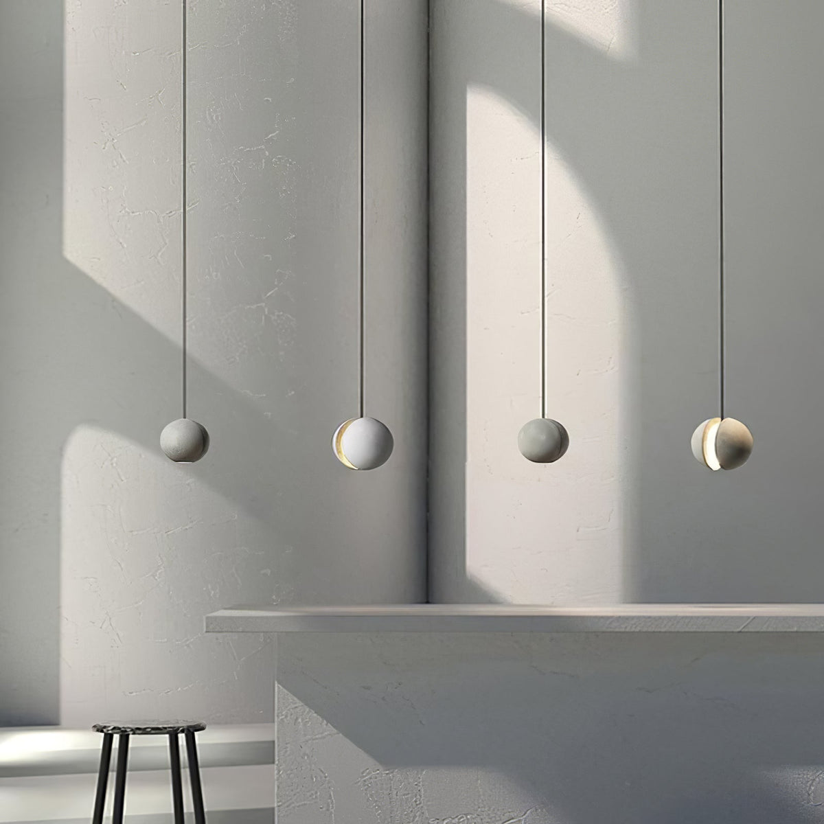 Four Clérachic spheres hang in a line before a rounded grey wall, with a stool and a pale counter in the lower corner.