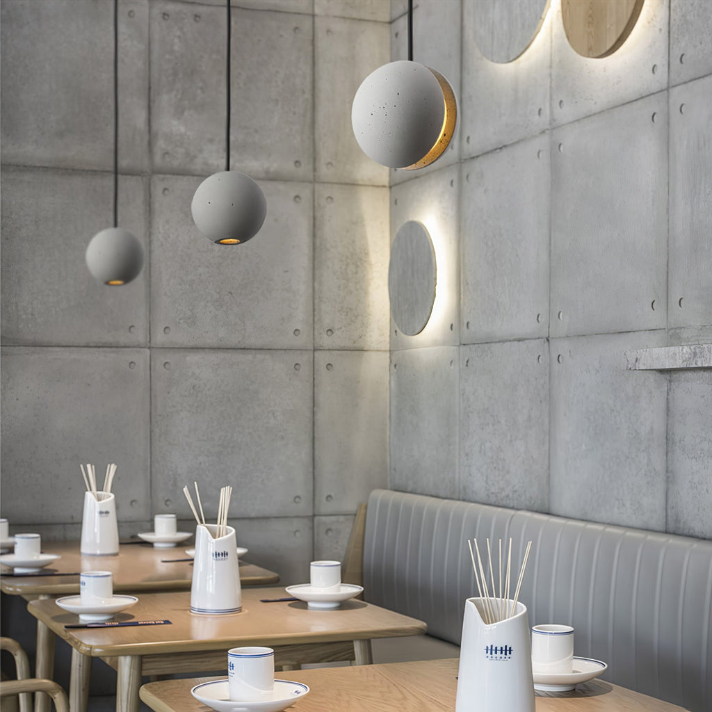 Three Clérachic concrete pendants hang in a corner of a restaurant with panelled concrete walls and wooden tables.