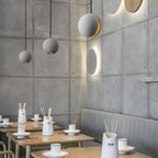 Three Clérachic concrete pendants hang in a corner of a restaurant with panelled concrete walls and wooden tables.