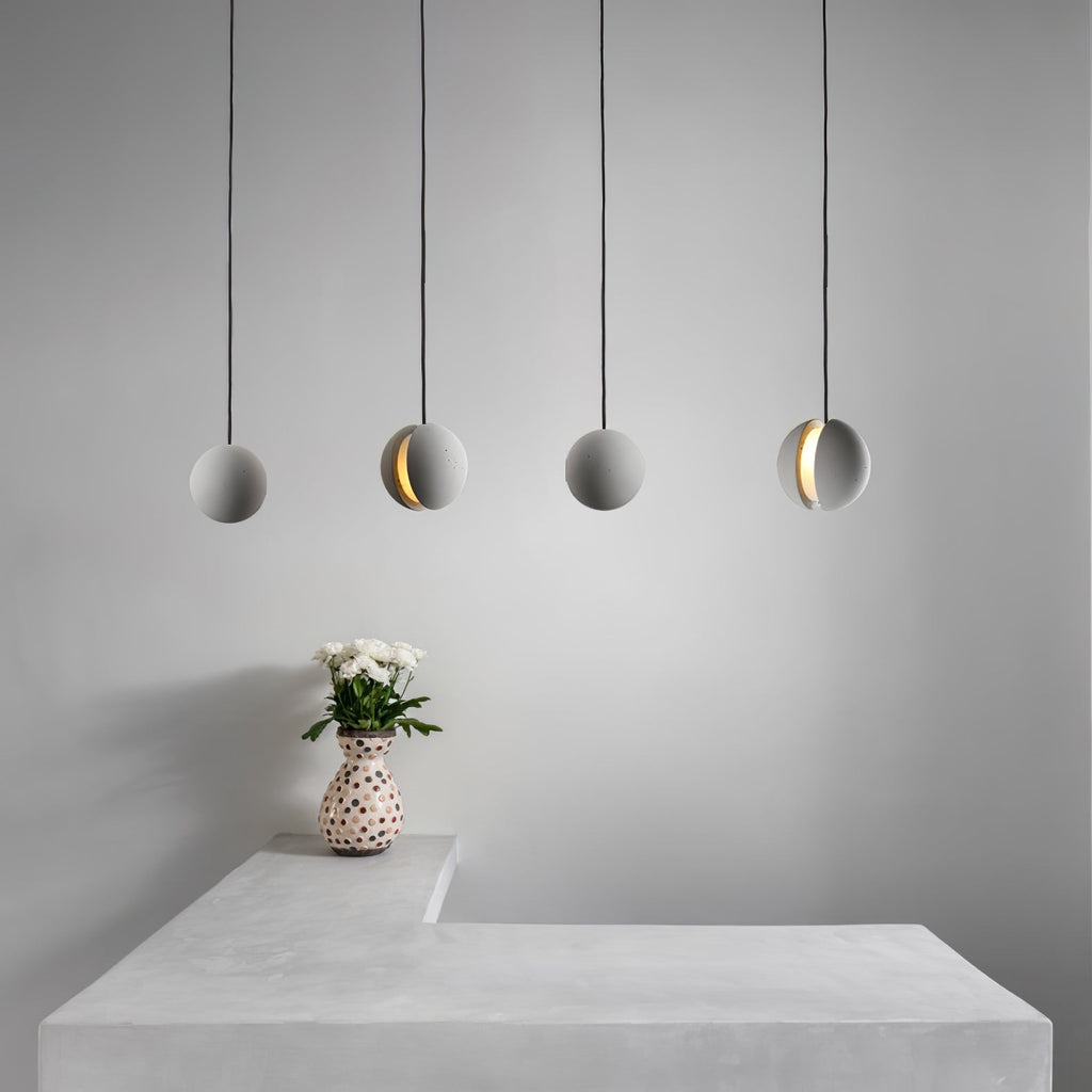 Four Clérachic spheres hang in a row over a pale concrete counter, with a spotted vase of white blooms beneath them.