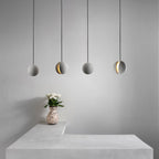Four Clérachic spheres hang in a row over a pale concrete counter, with a spotted vase of white blooms beneath them.