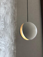 Close view of a Clérachic concrete pendant, its crescent slot glowing warm against a pale mottled wall.