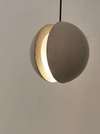 Close view of the crescent opening on this Clérachic pendant, showing the warm light inside the cement-grey shell.