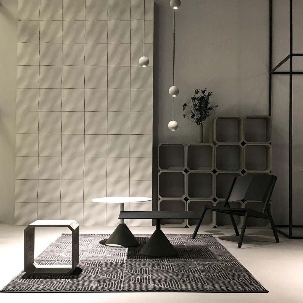 High in a concrete showroom, small Clérachic spheres hang on a long cord over low black tables and a patterned rug.