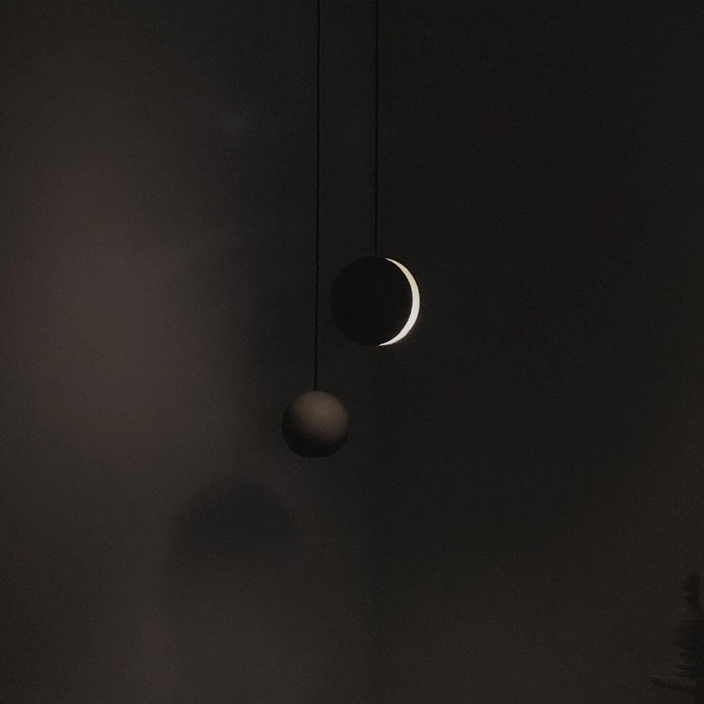 Two Clérachic concrete pendants hang in near darkness, one showing a thin bright crescent of light.