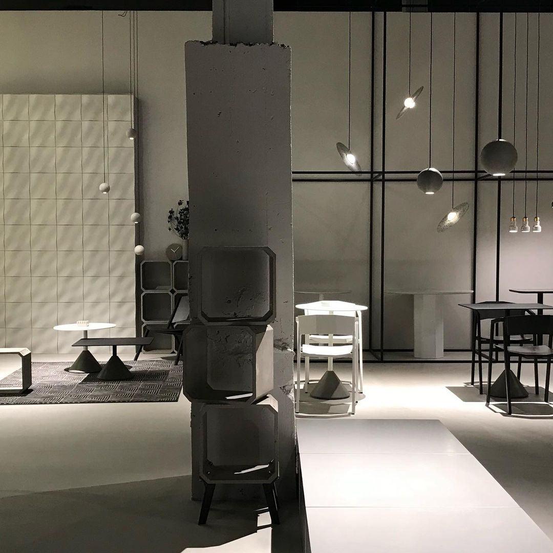 A Clérachic concrete pendant hangs in the distance of a dim showroom, past a column of stacked concrete cubes.