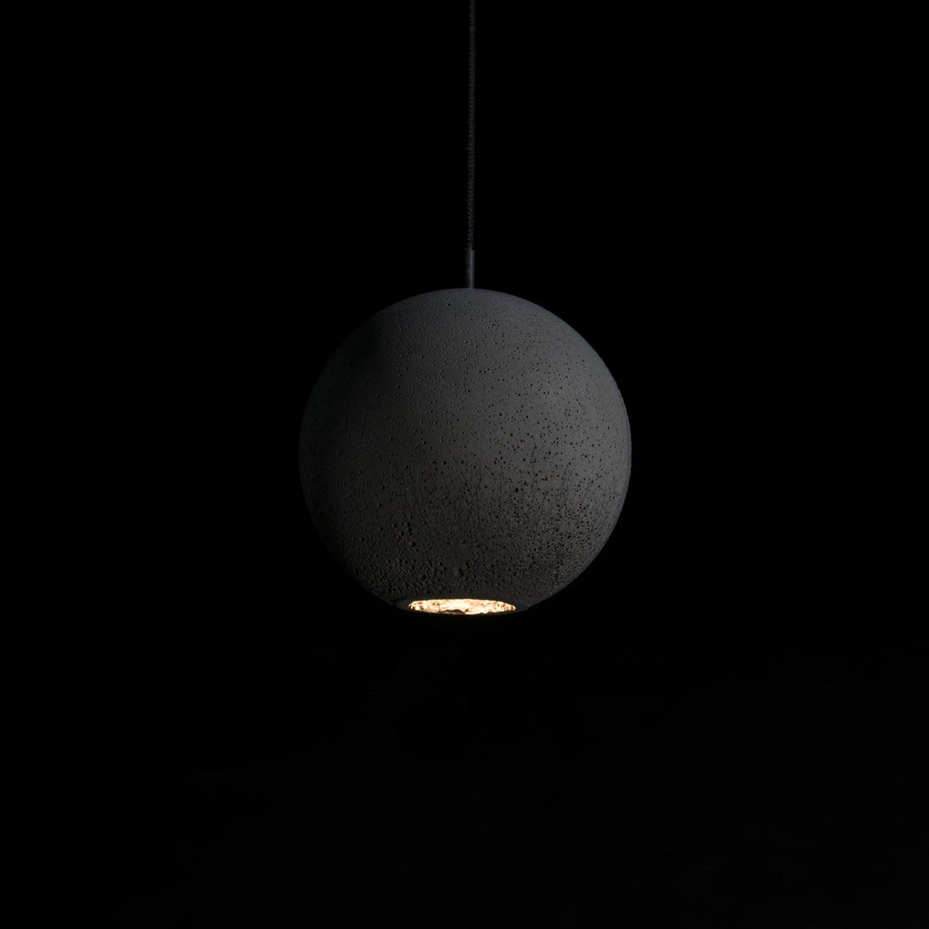 A large Clérachic concrete sphere hangs in the dark, its rough surface lit from a small opening at the base.