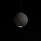 A large Clérachic concrete sphere hangs in the dark, its rough surface lit from a small opening at the base.