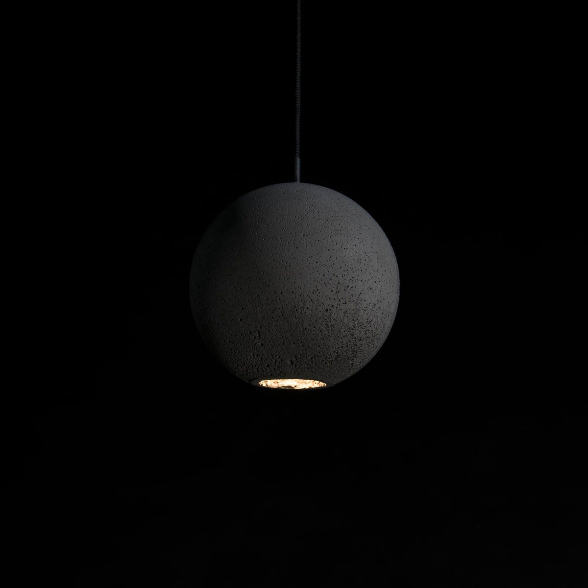 A large Clérachic concrete sphere hangs in the dark, its rough surface lit from a small opening at the base.