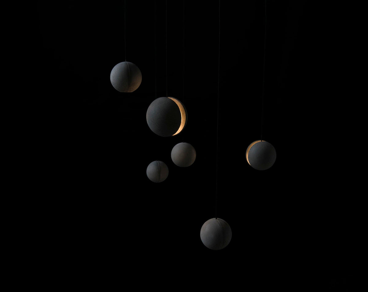 Seven Clérachic concrete spheres of different sizes float in a black space, a few of them glowing through a slot.