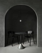 A tiny Clérachic sphere hangs inside a stone archway over a small round table and two black chairs on a grey floor.
