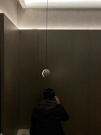 A lit Clérachic concrete pendant hangs against a dark wood-panelled wall with a strip of light along the ceiling.