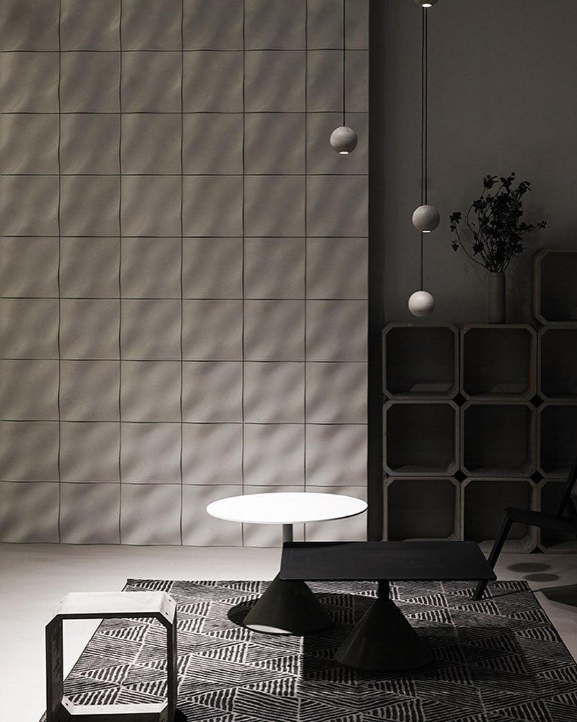 Three Clérachic spheres hang at different heights beside a tiled wall and shelving, above low black tables.