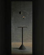 Two Clérachic concrete pendants hang in a dark doorway, one with a visible crescent glow, over a tall dark table.