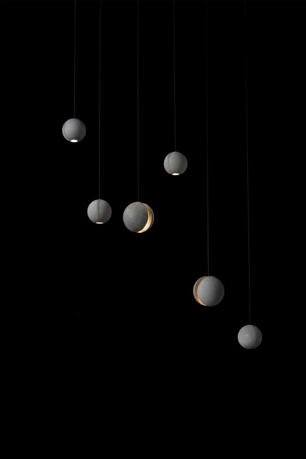 Six Clérachic concrete spheres hang at varied heights against black, each with a small warm glow at the base or slot.