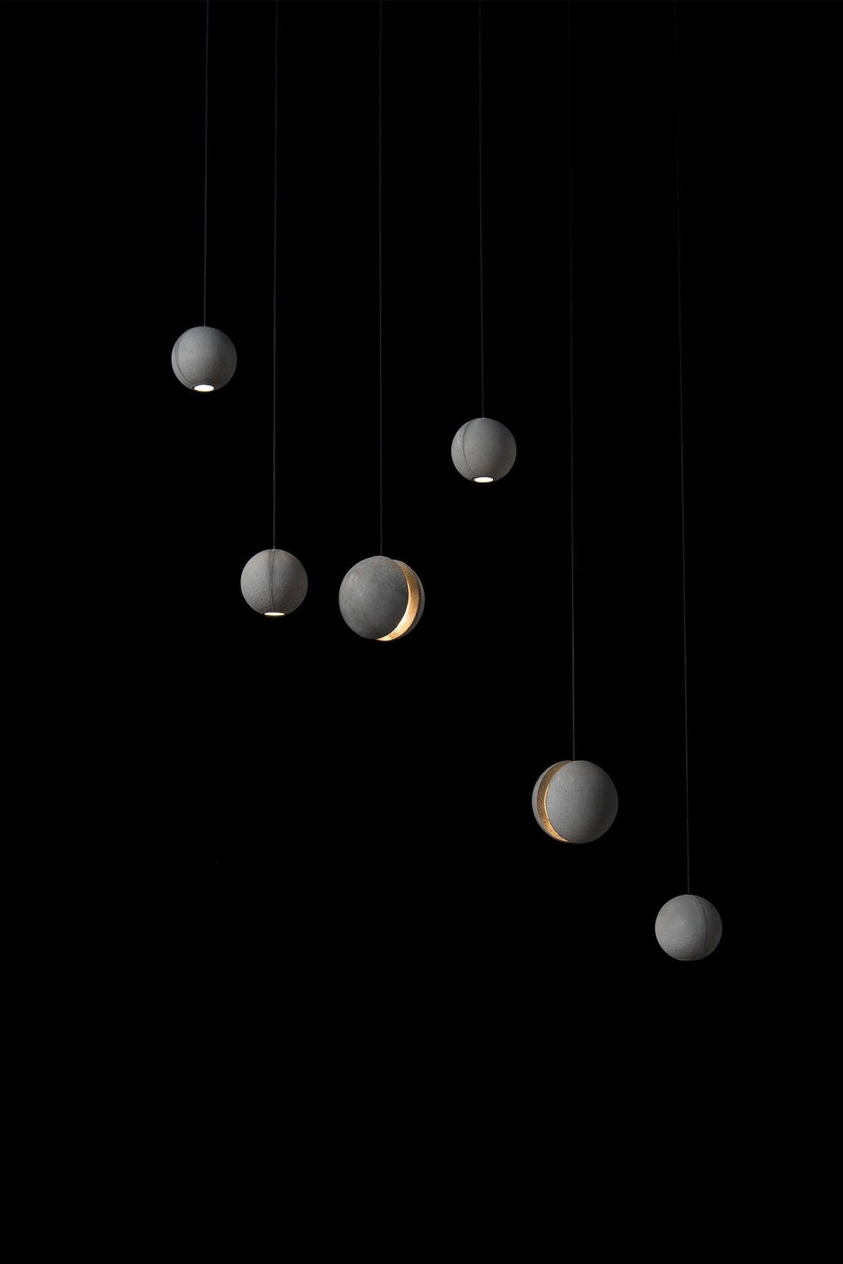 Six Clérachic concrete spheres hang at varied heights against black, each with a small warm glow at the base or slot.