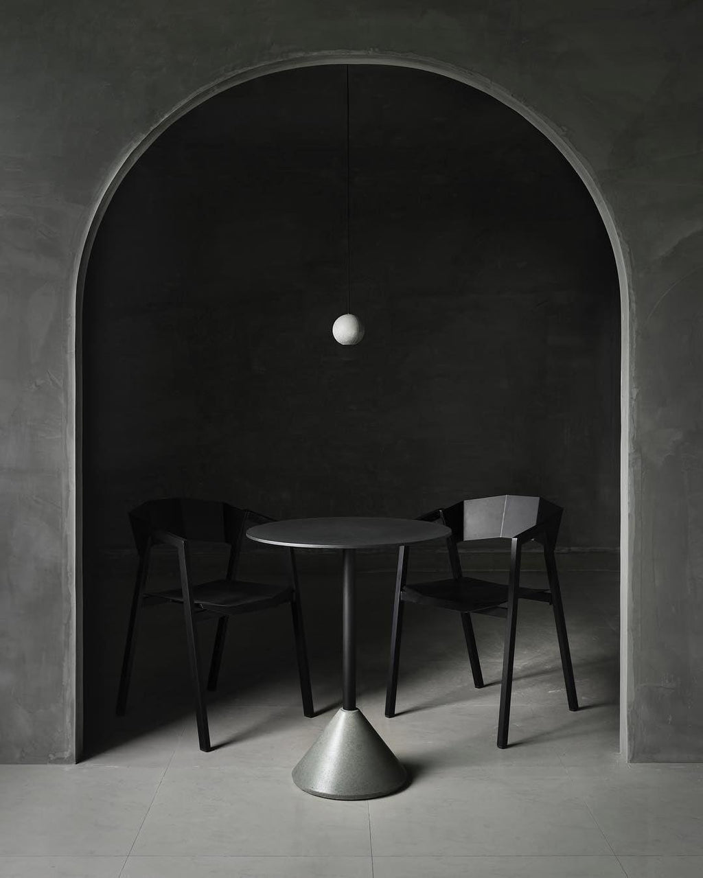 A small pale Clérachic sphere hangs under an arched alcove above a cone-based table and two black chairs.