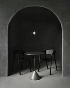 A small pale Clérachic sphere hangs under an arched alcove above a cone-based table and two black chairs.