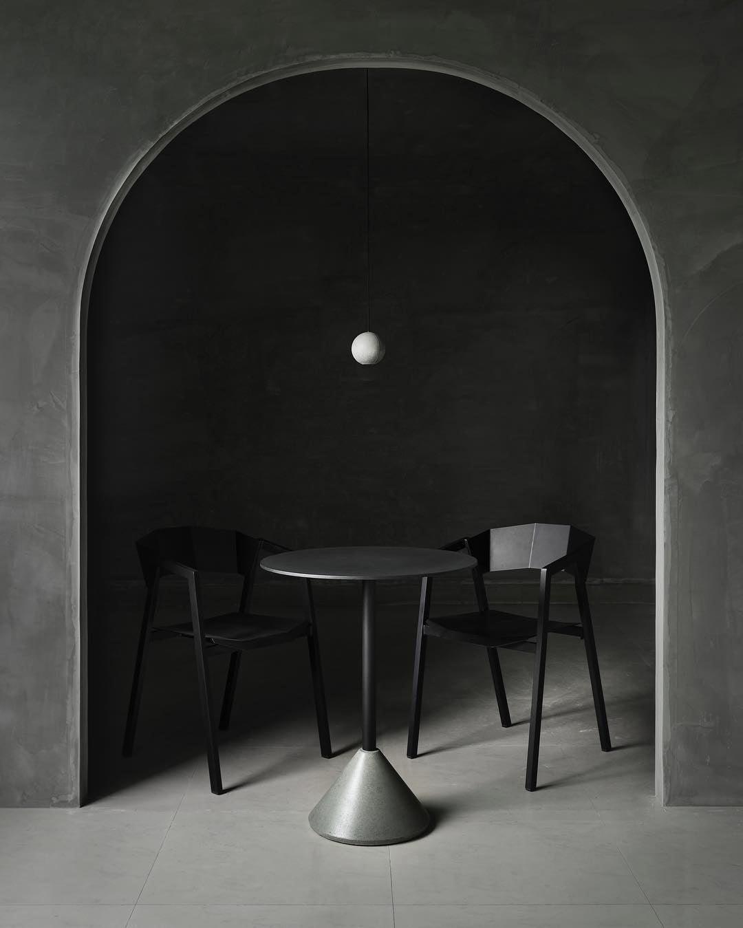A small pale Clérachic sphere hangs under an arched alcove above a cone-based table and two black chairs.