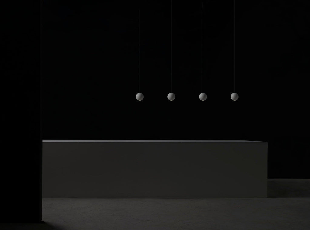 Four small Clérachic spheres hang in a line in a dark room above a long, low concrete block.