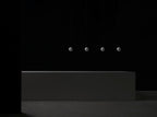Four small Clérachic spheres hang in a line in a dark room above a long, low concrete block.