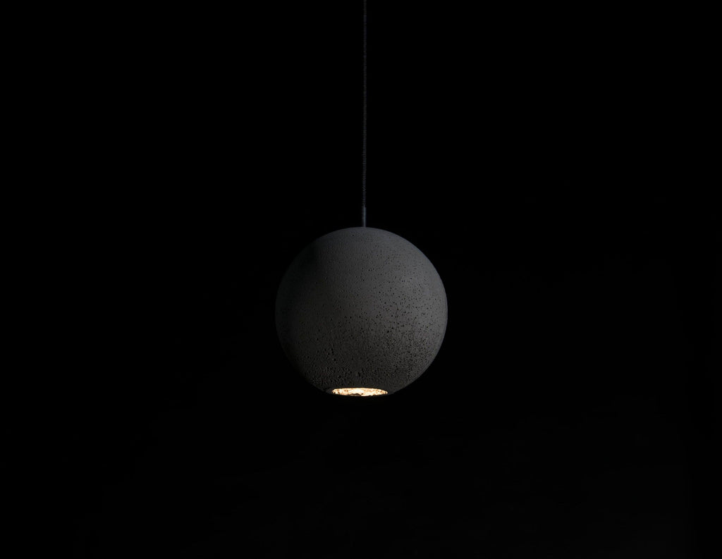 A Clérachic concrete sphere hangs in the dark with a warm pool of light escaping from its base.