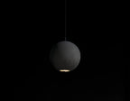 A Clérachic concrete sphere hangs in the dark with a warm pool of light escaping from its base.