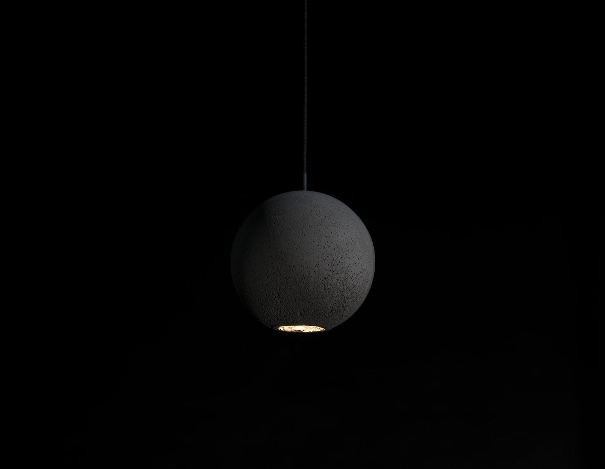 A Clérachic concrete sphere hangs in the dark with a warm pool of light escaping from its base.