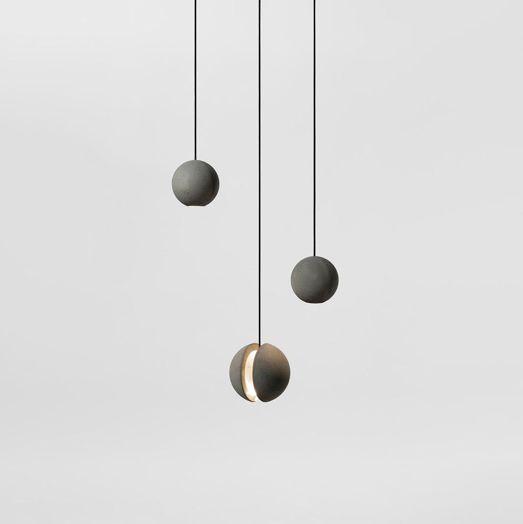 Three Clérachic concrete pendants hang at different heights against a pale grey backdrop, the lowest showing its lit slot.