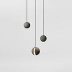 Three Clérachic concrete pendants hang at different heights against a pale grey backdrop, the lowest showing its lit slot.