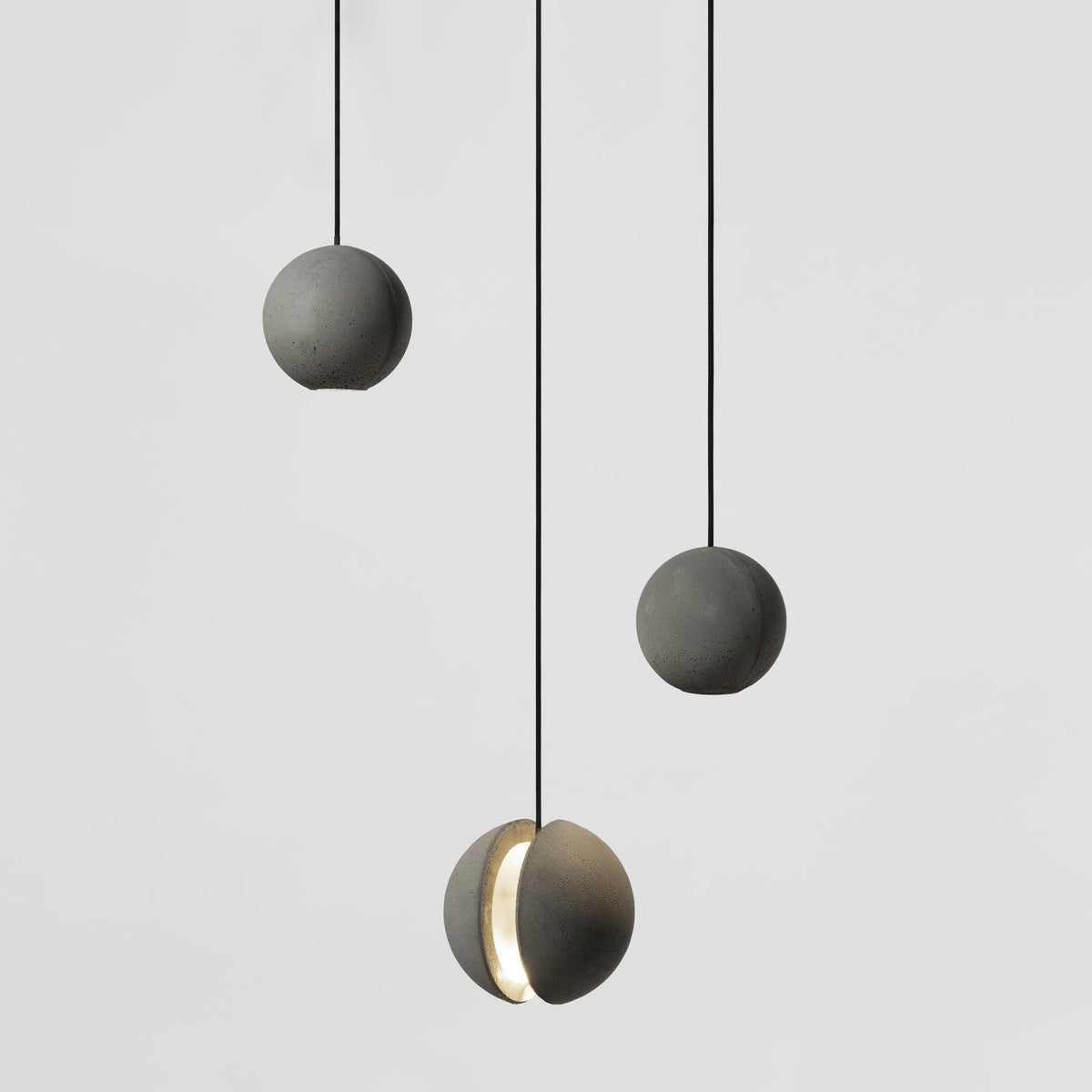 Three Clérachic concrete spheres hang against a light grey backdrop, two plain and the lowest with a glowing crescent.