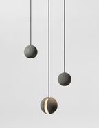 Three smaller Clérachic concrete pendants hang on black cords in a grey studio, the lowest lit through its slot.