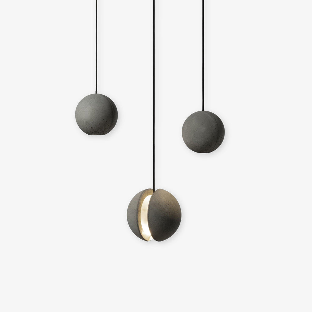 Three Clérachic pendants hang close together on a white backdrop, the lowest with its slot glowing warm.