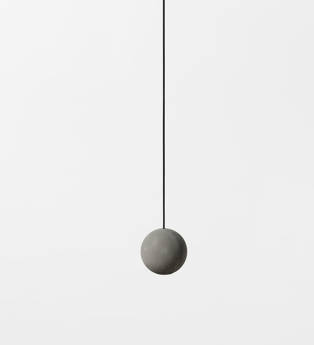 A single plain cement-grey Clérachic sphere hangs on a thin black cord against a pale backdrop.