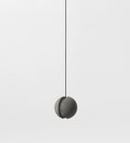 A Clérachic concrete pendant with a closed crescent slot hangs on a black cord against a pale backdrop, unlit.