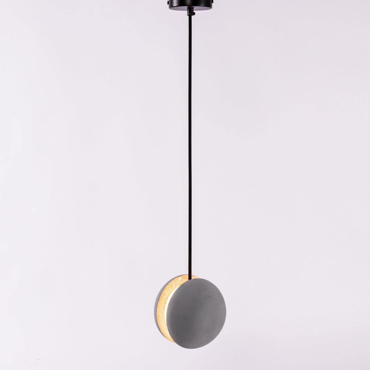 A Clérachic pendant shown straight on from a black canopy, a warm crescent of light along one edge.