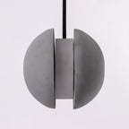 Front view of the split Clérachic concrete pendant, two grey halves parted around a central cylinder.