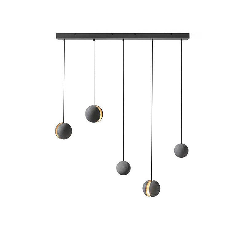 Five Clérachic concrete pendants hang from a long black canopy on white, two with a glowing slot, at staggered heights.