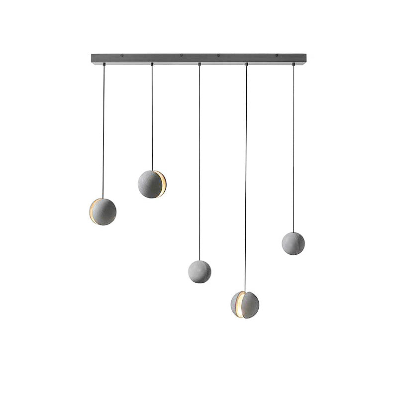 Five Clérachic concrete pendants hang at staggered drops from a long black bar canopy, three with lit slots.