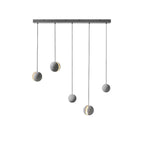 Five Clérachic concrete pendants hang at staggered drops from a long black bar canopy, three with lit slots.