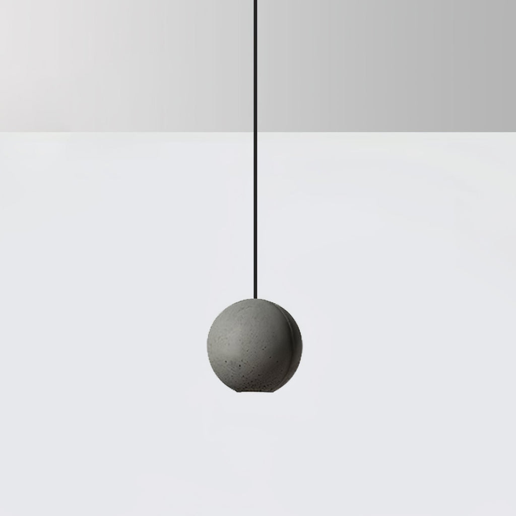 A cement-grey Clérachic sphere pendant hangs on a black cord against a pale grey wall and white floor.