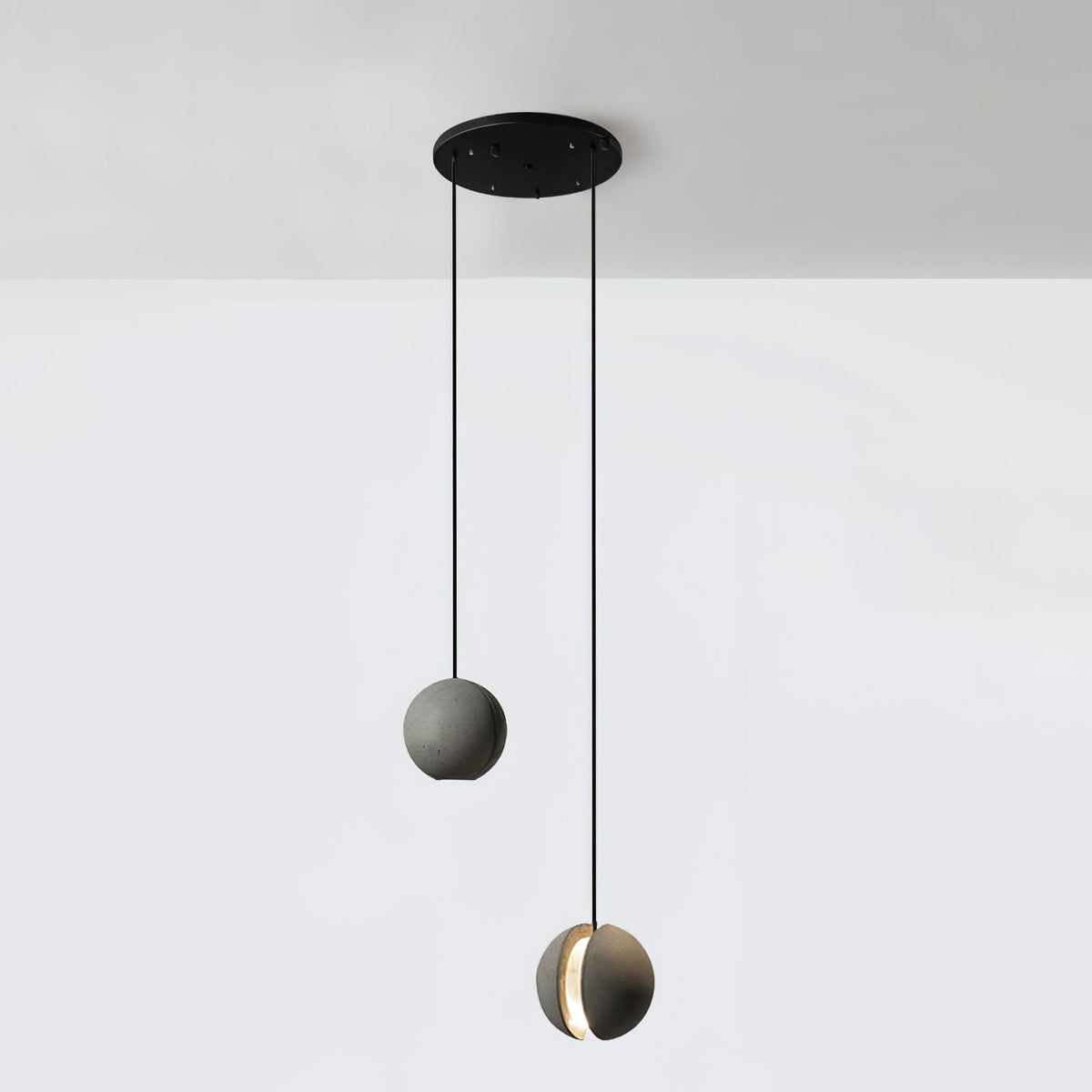 Two Clérachic concrete pendants hang from a round black canopy at different heights against a white wall.