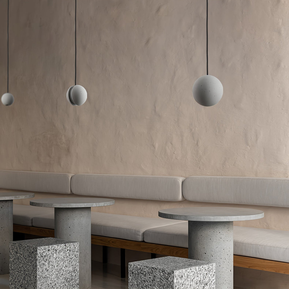 Three Clérachic concrete pendants hang against a sand-coloured plaster wall above banquette seating and stone tables.