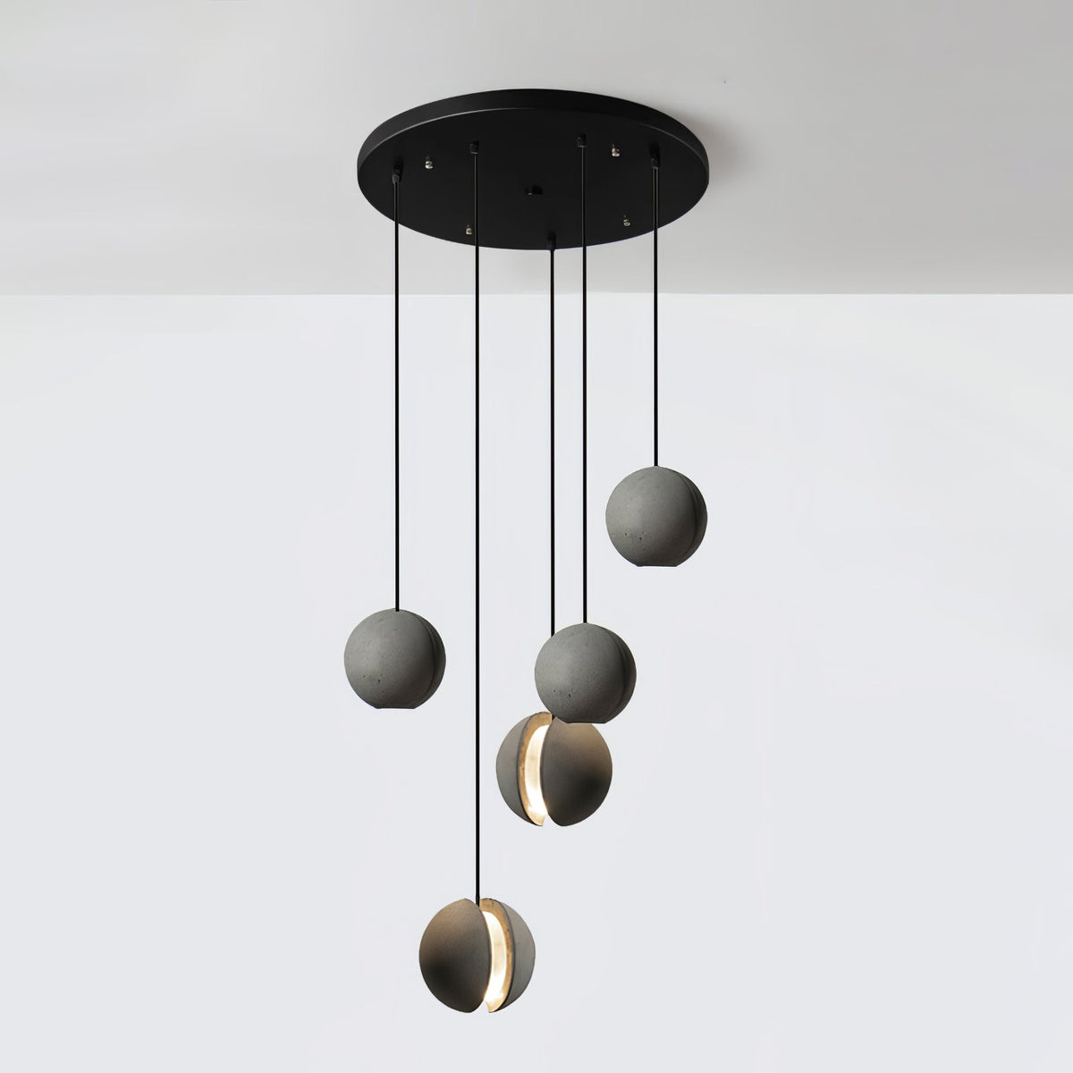 Five Clérachic concrete pendants hang from a wide round black canopy at staggered heights against a white wall.