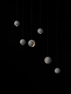 Six Clérachic concrete spheres hang at staggered heights on black, a few with a lit slot and others a light at the base.