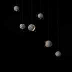 Six Clérachic concrete pendants hang against black, three with a glow at the base and two with a lit crescent.
