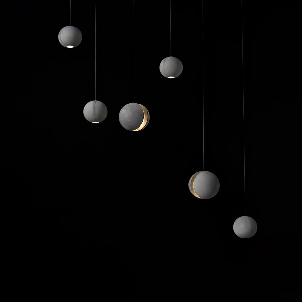 Six Clérachic concrete pendants hang against black, three with a glow at the base and two with a lit crescent.