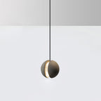 A Clérachic concrete pendant glows through its crescent slot, hanging against a pale wall above a white floor.
